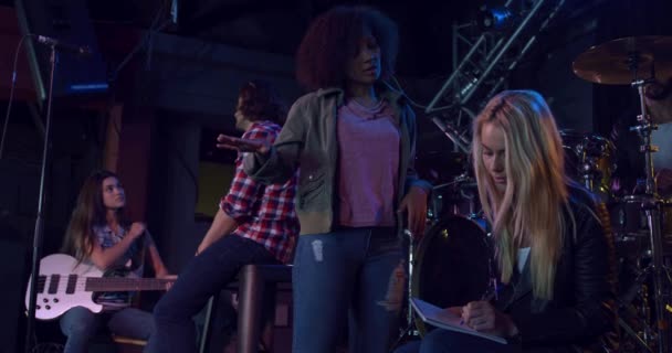 Front view of a group of four multi-ethnic male and female musicians having fun together before performing, discussing, playing guitar, one girl is making notes, interacting in slow motion - Materiał filmowy, wideo