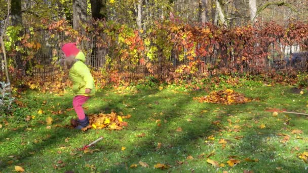 Stoute kleine meid schopt geharkte bladeren in de tuin. Gek kind stoeien in tuin - Video
