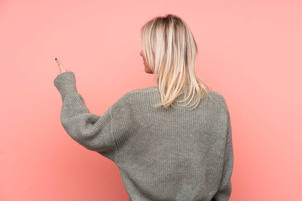 Young blonde Russian woman over isolated pink background pointing back with the index finger - Foto, Imagen