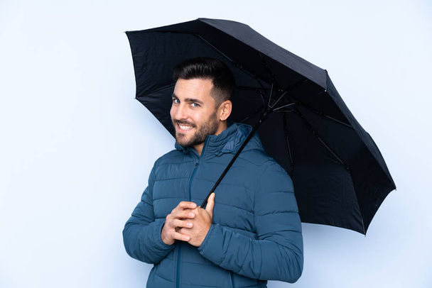 Άντρας που κρατάει ομπρέλα πάνω από απομονωμένο φόντο χαμογελώντας πολύ - Φωτογραφία, εικόνα
