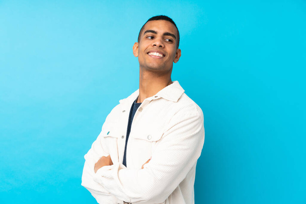 Young African American man over isolated blue background with arms crossed and happy - Foto, Imagen