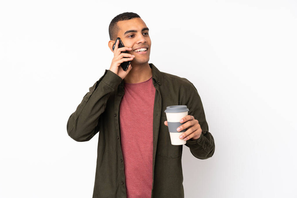 Jeune Afro-Américain sur fond blanc isolé tenant du café à emporter et un mobile - Photo, image