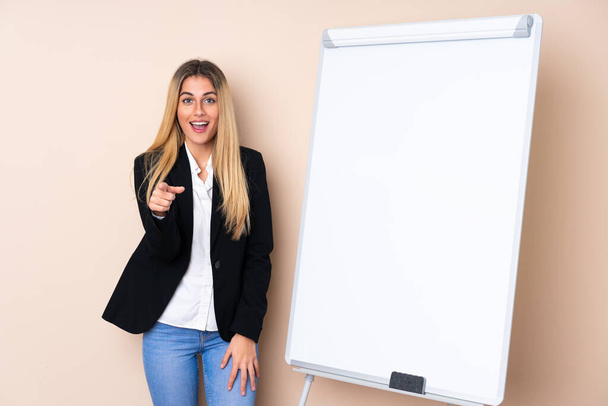 Young Uruguayan woman giving a presentation on white board and surprised while pointing front - Photo, Image