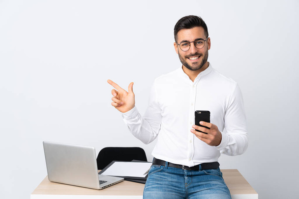 Молодой бизнесмен держит мобильный телефон, указывая пальцем в сторону
 - Фото, изображение