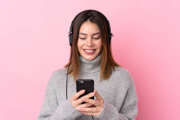 Jovem mulher ouvindo música com fones de ouvido sobre parede rosa isolada
 - Foto, Imagem