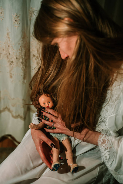 Girl in night gown holding old dolls in her hands. Bizarre, disturbing concept - Foto, imagen