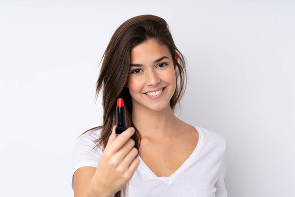Adolescente chica sobre aislado fondo sosteniendo rojo lápiz labial y ofreciéndolo
 - Foto, Imagen