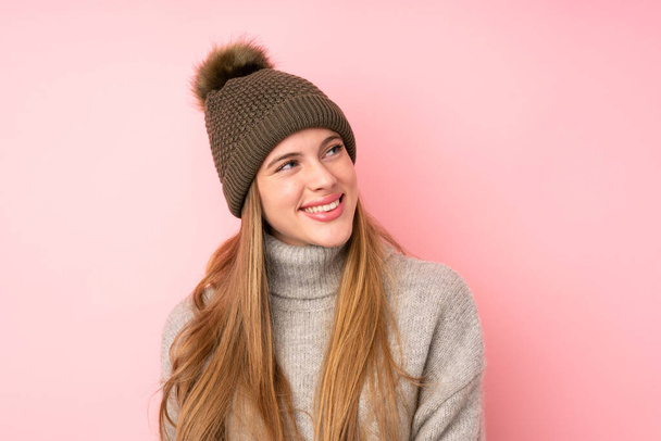 Young teenager girl with winter hat over isolated pink background laughing and looking up - Fotoğraf, Görsel