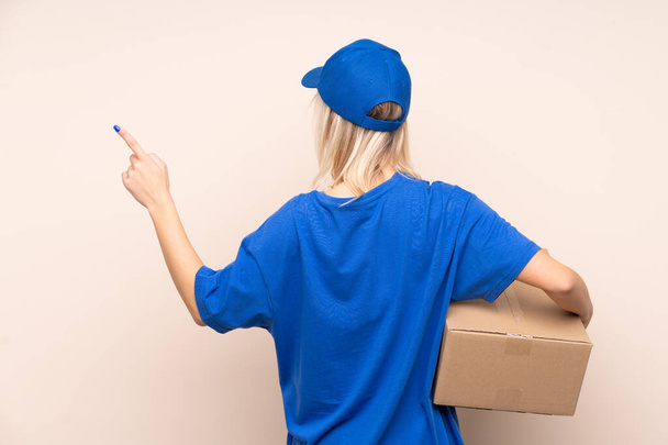 Young delivery woman over isolated background pointing back with the index finger - Photo, Image