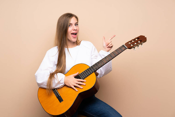 Teenager girl with guitar over isolated background surprised and pointing finger to the side - Foto, Bild