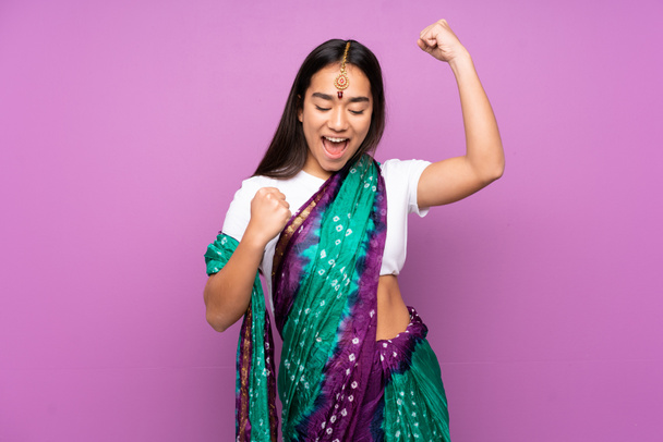 Νεαρή Ινδή γυναίκα με σάρι πάνω σε απομονωμένο φόντο γιορτάζει μια νίκη - Φωτογραφία, εικόνα
