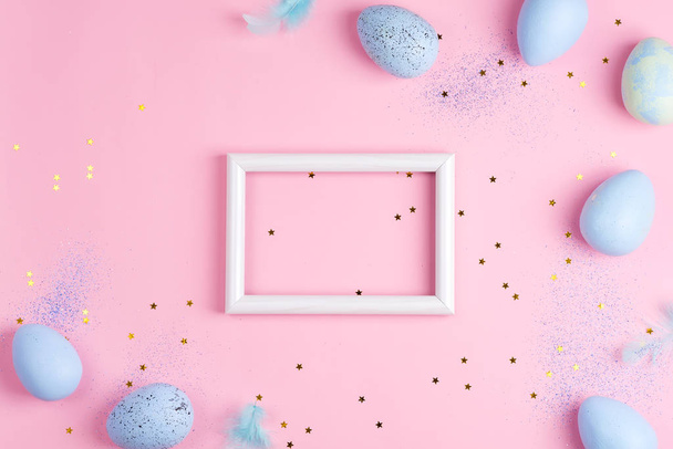Moldura festiva com ovos pintados de cores azuis pastel e decoração de confetes em um fundo rosa claro
. - Foto, Imagem