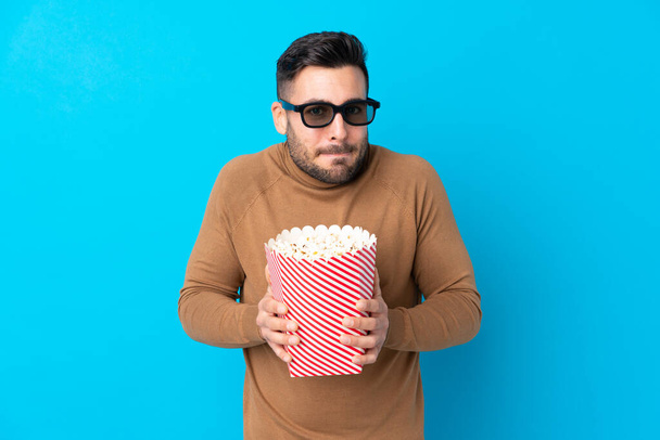 Młody przystojny mężczyzna w okularach 3D i trzymający duży kubeł popcornu - Zdjęcie, obraz