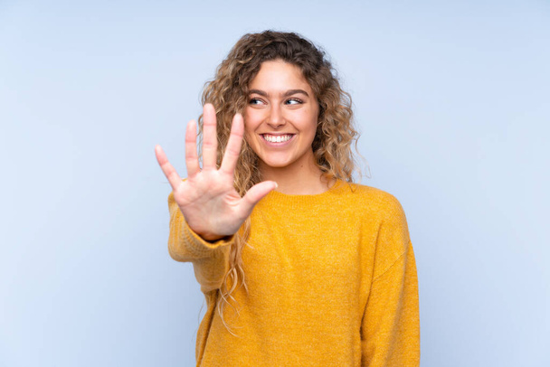 Young blonde woman with curly hair isolated on blue background counting five with fingers - Photo, Image