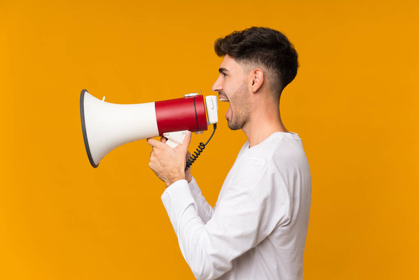 Young man over isolated orange background shouting through a megaphone - Photo, Image