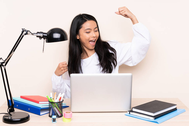 Студентська азіатська дівчина на робочому місці з ноутбуком ізольовано на бежевому фоні, що святкує перемогу
 - Фото, зображення