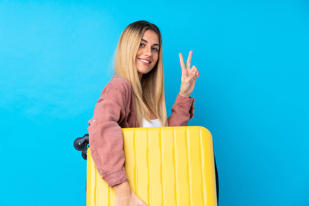 Young Uruguayan woman over isolated blue background in vacation with travel suitcase and making victory gesture - Foto, Bild