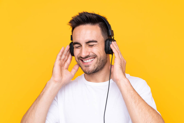Young man over yellow background listening music and singing - Zdjęcie, obraz