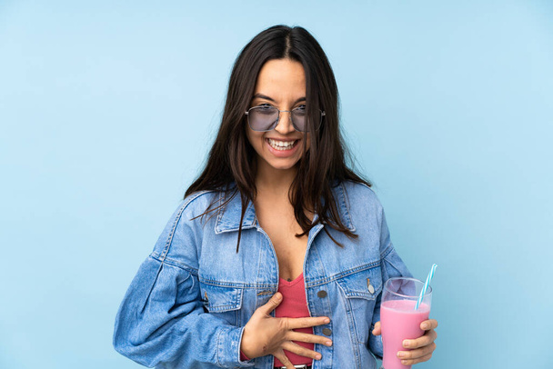 Jeune femme avec milkshake fraise sur fond bleu isolé souriant beaucoup
 - Photo, image