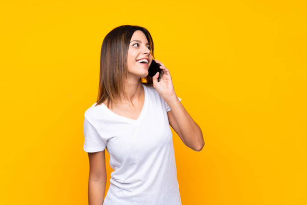 junge Frau auf isoliertem gelben Hintergrund führt ein Gespräch mit dem Handy - Foto, Bild