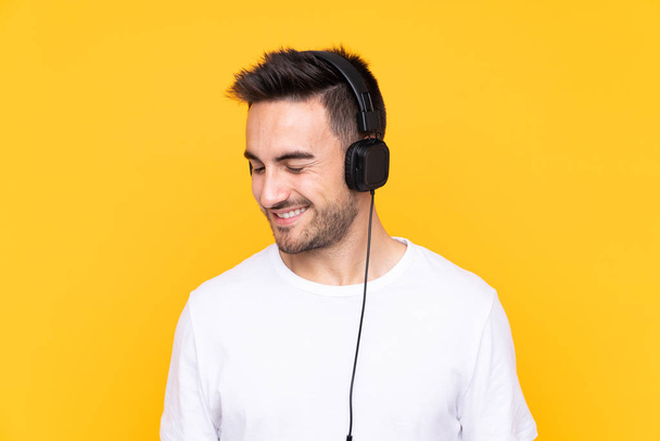 Young man over yellow background listening music - Photo, Image