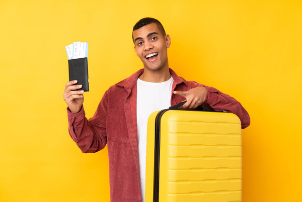 若いですアフリカ系アメリカ人男性以上隔離された黄色の背景で休暇でスーツケースとパスポートと驚き - 写真・画像
