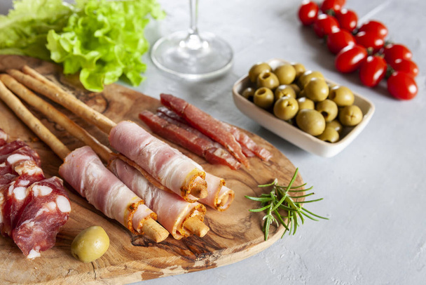 Set of smoked bacon, salami and basturma served with pickled olives, tomatoes, wine and grissini bread. Close up on white background - Фото, зображення