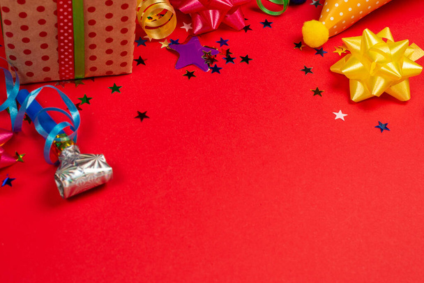 Estrellas festivas doradas y púrpuras de confeti y un regalo, gorras de cumpleaños sobre un fondo rojo. Espacio para texto o diseño
. - Foto, Imagen