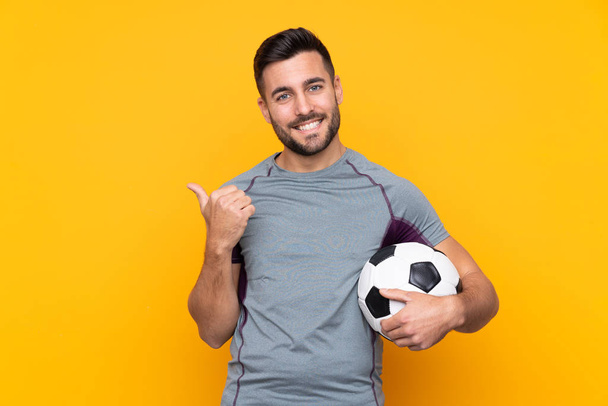 Voetbalspeler man over geïsoleerde achtergrond wijst naar de zijkant om een product te presenteren - Foto, afbeelding