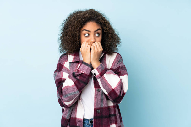 Young African American woman isolated on blue background nervous and scared putting hands to mouth - 写真・画像