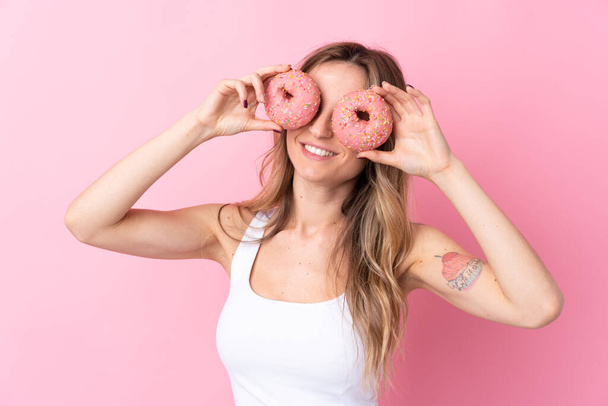 Young woman over isolated pink background holding donuts in eyes - Фото, изображение