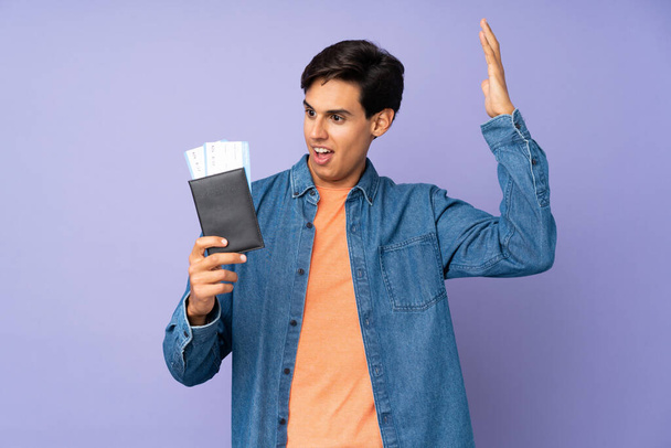 Man over isolated purple background in vacation with plane tickets and surprised - Photo, image