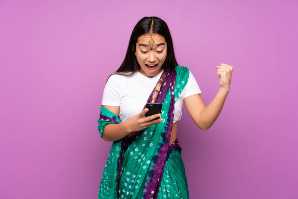 Young Indian woman with sari over isolated background surprised and sending a message - Photo, Image