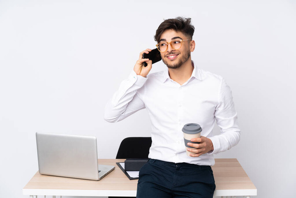 Araber in einem Büro isoliert auf weißem Hintergrund mit Kaffee zum Mitnehmen und einem Handy - Foto, Bild