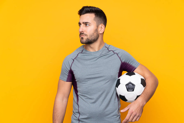 Man over geïsoleerde gele achtergrond met voetbal - Foto, afbeelding