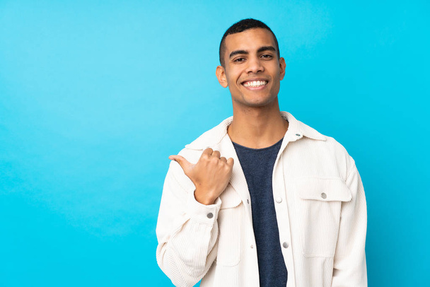 Junger afroamerikanischer Mann über isoliertem blauem Hintergrund, der zur Seite zeigt, um ein Produkt zu präsentieren - Foto, Bild