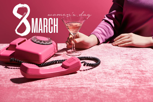 oříznutý pohled ženy držící sklenici růžového vína u retro telefonu na sametové látce izolované na růžové, 8 březen ilustrace - Fotografie, Obrázek