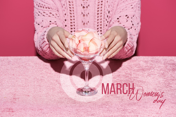 περικοπή άποψη της γυναίκας με πέταλα σε γυαλί σε βελούδο ύφασμα που απομονώνονται σε ροζ, 8 Μαρτίου εικονογράφηση - Φωτογραφία, εικόνα