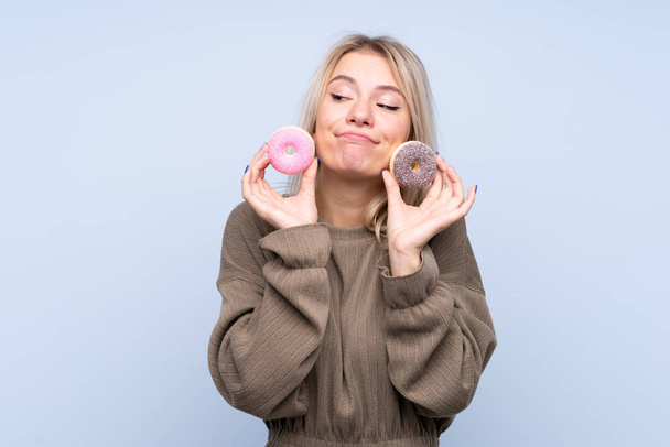 Young blonde woman over isolated blue background holding donuts - Photo, Image