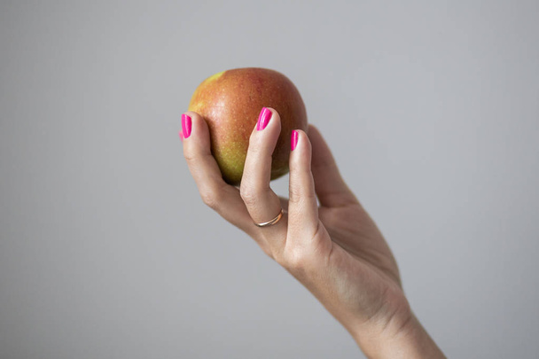 Female hands with perfect pink manicure hold an apple, concept photo - Photo, image