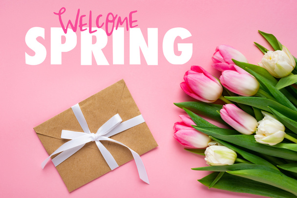 Top view of envelope with bow and bouquet of tulips on pink surface, welcome spring illustration - Photo, Image