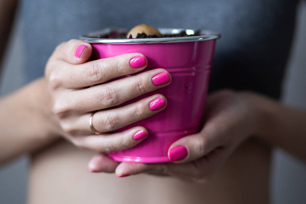 Woman holds a pink flower pot with avocado sprout over her belly. Conceptual photo - 写真・画像