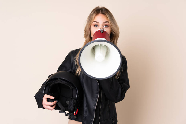 Russian girl with a motorcycle helmet isolated on beige background shouting through a megaphone - Fotoğraf, Görsel