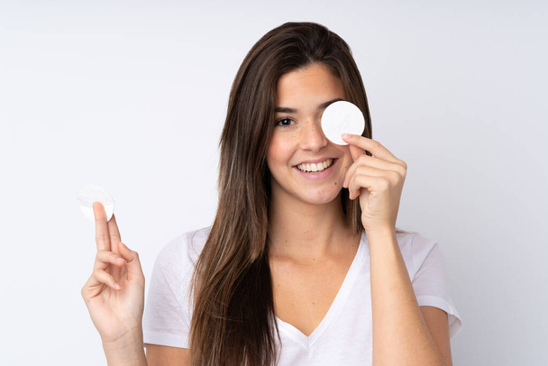 Teenager girl over isolated background with cotton pad for removing makeup from her face and smiling - Photo, Image