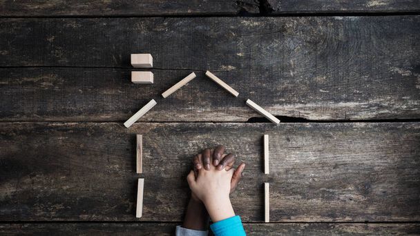 Equality and peace conceptual image - hand of caucasian and colored child holding each other inside a house made of ooden pegs. Over wooden background. - Photo, Image