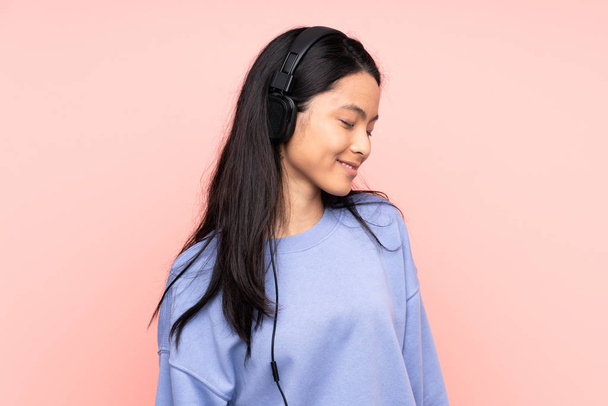 Teenager Chinese girl isolated on pink background listening music - Zdjęcie, obraz