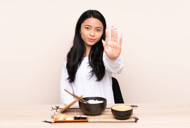 Teenager Asian girl eating asian food isolated on beige background making stop gesture - Photo, Image