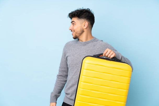 Arab jóképű férfi elszigetelt kék háttér nyaralás utazási bőrönd - Fotó, kép