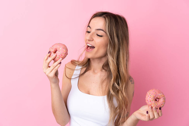 Jovem mulher sobre isolado fundo rosa segurando donuts com expressão feliz - Foto, Imagem