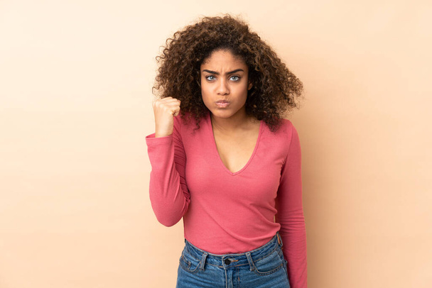 Young African American woman isolated on beige background with unhappy expression - Foto, Imagem
